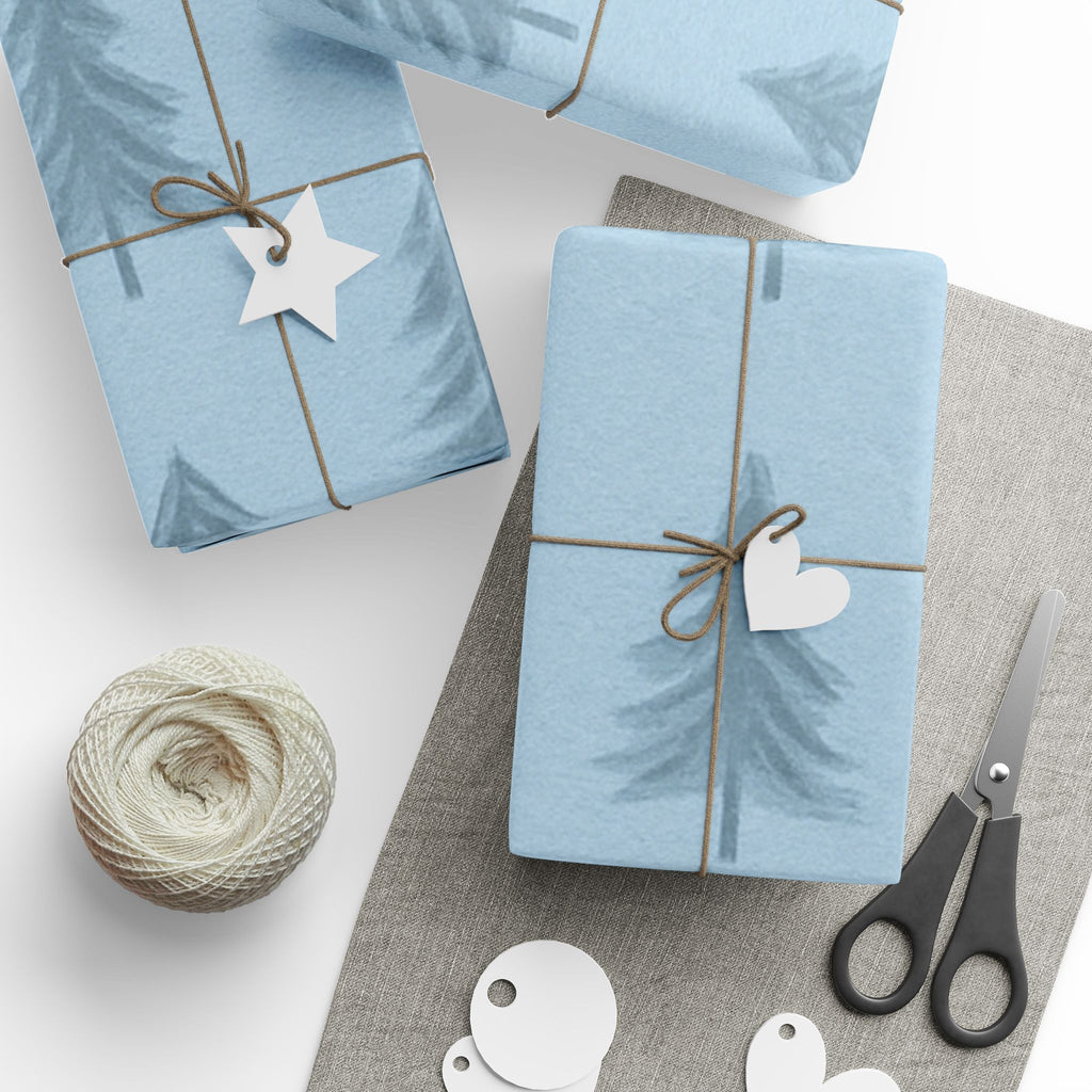 Two blue gift boxes with decorative tags on a white surface with scissors and yarn.