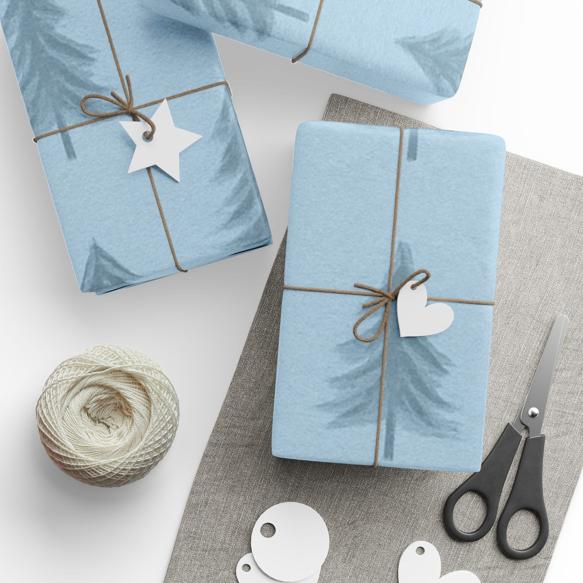 Two blue gift boxes with decorative tags on a white surface with scissors and yarn.