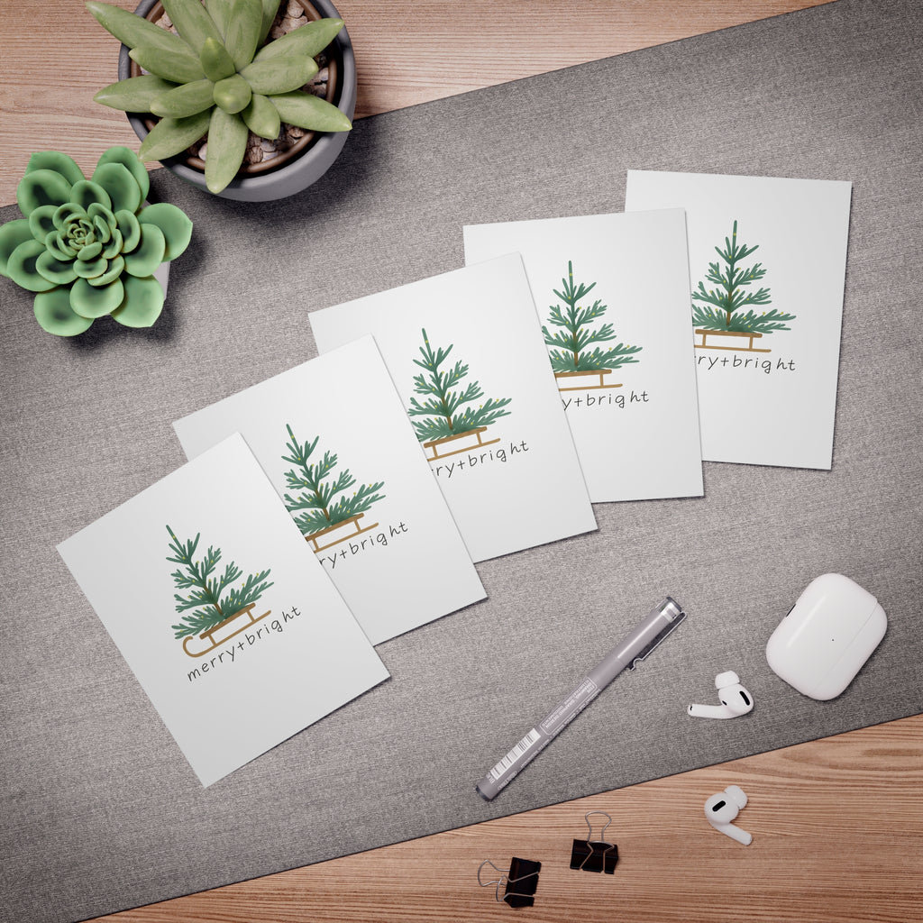 Set of greeting cards with Christmas tree designs on a desk with office supplies.